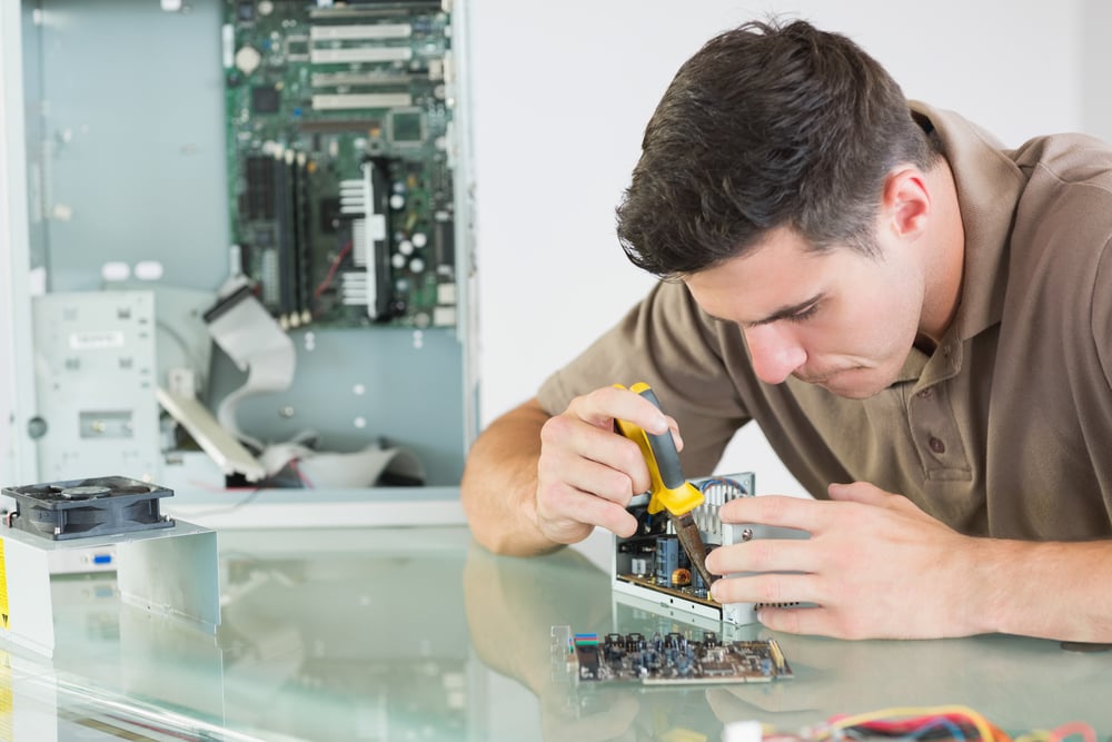 Handsome serious computer engineer repairing hardware with pliers in bright office